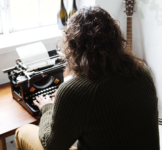 På bilden syns Christoffer Hidings rygg. Han sitter vid ett skrivbord och skriver på en gammal skrivmaskin.
